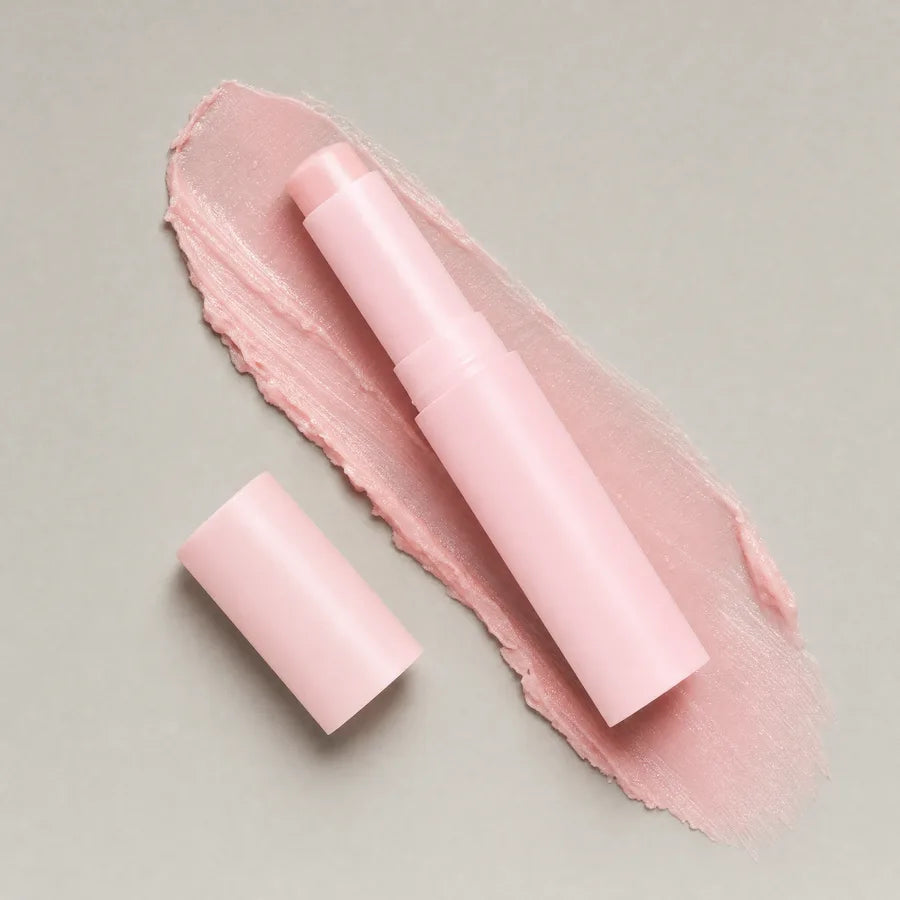 Overhead view of the pink balm stick lying open beside its cap on a swatch of balm