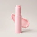 Pink twist-up multi balm stick standing upright beside a swatch of the pale pink balm